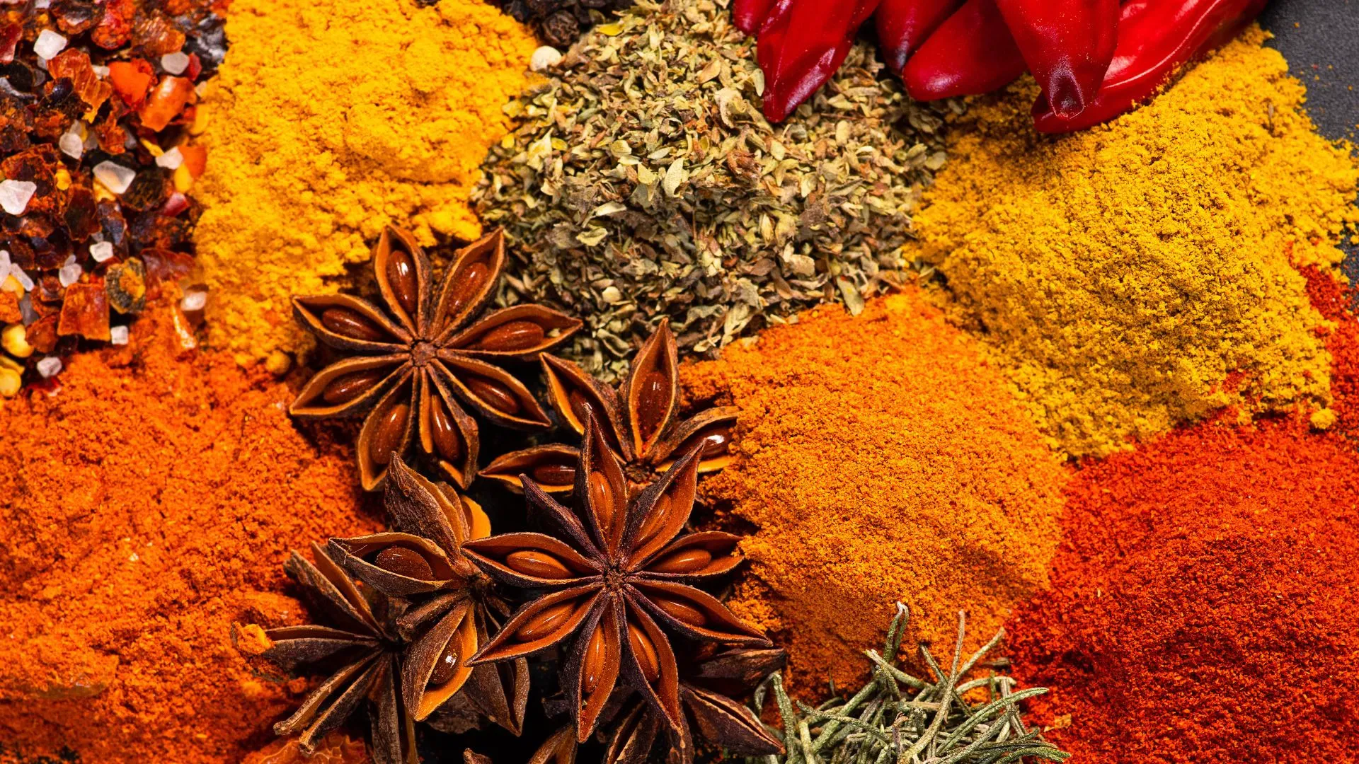 Piles of colorful ground spices with star anise pods, dried red chilies, and dried herbs
