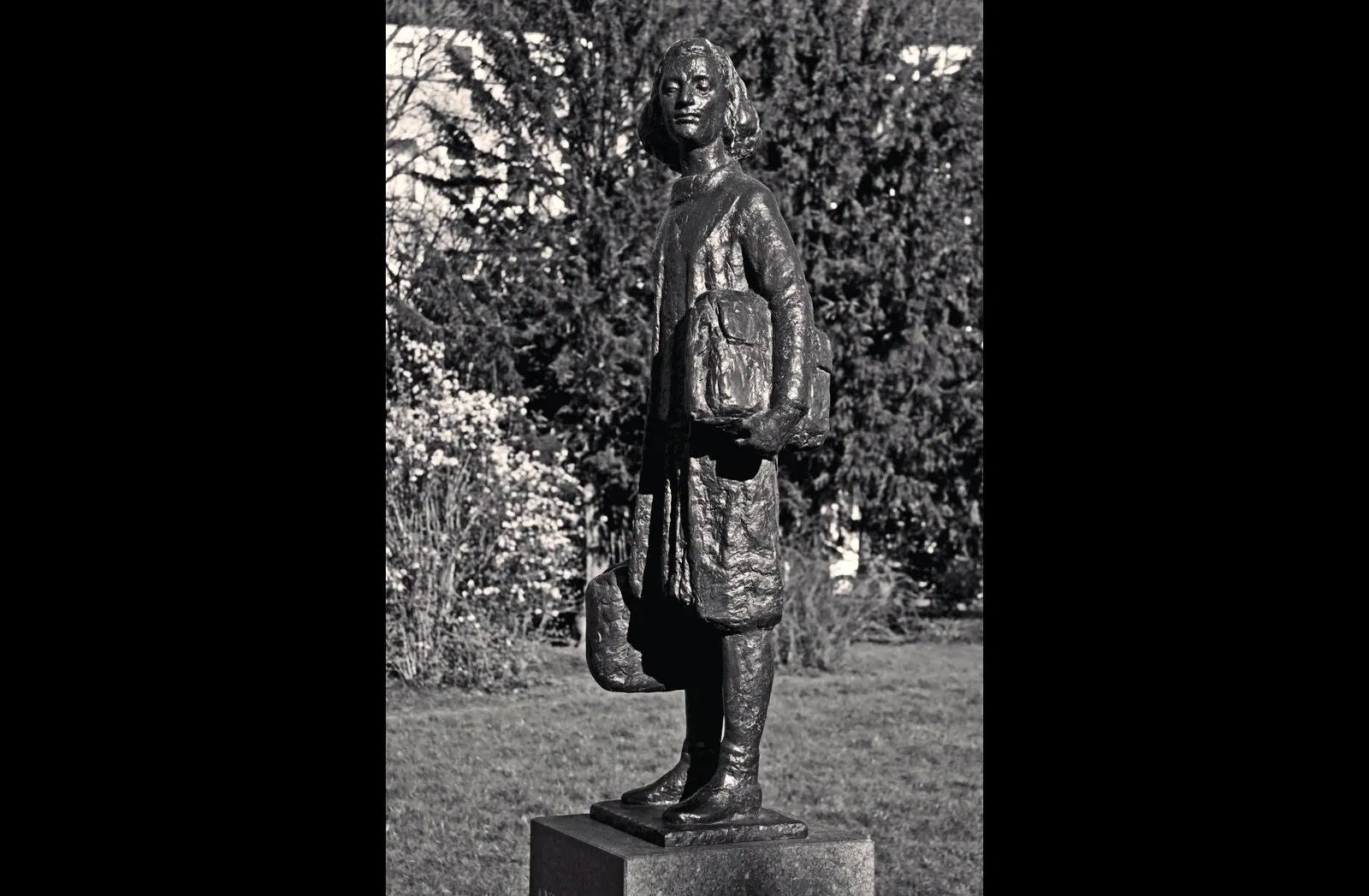Bronze statue of Anne Frank standing in a garden
