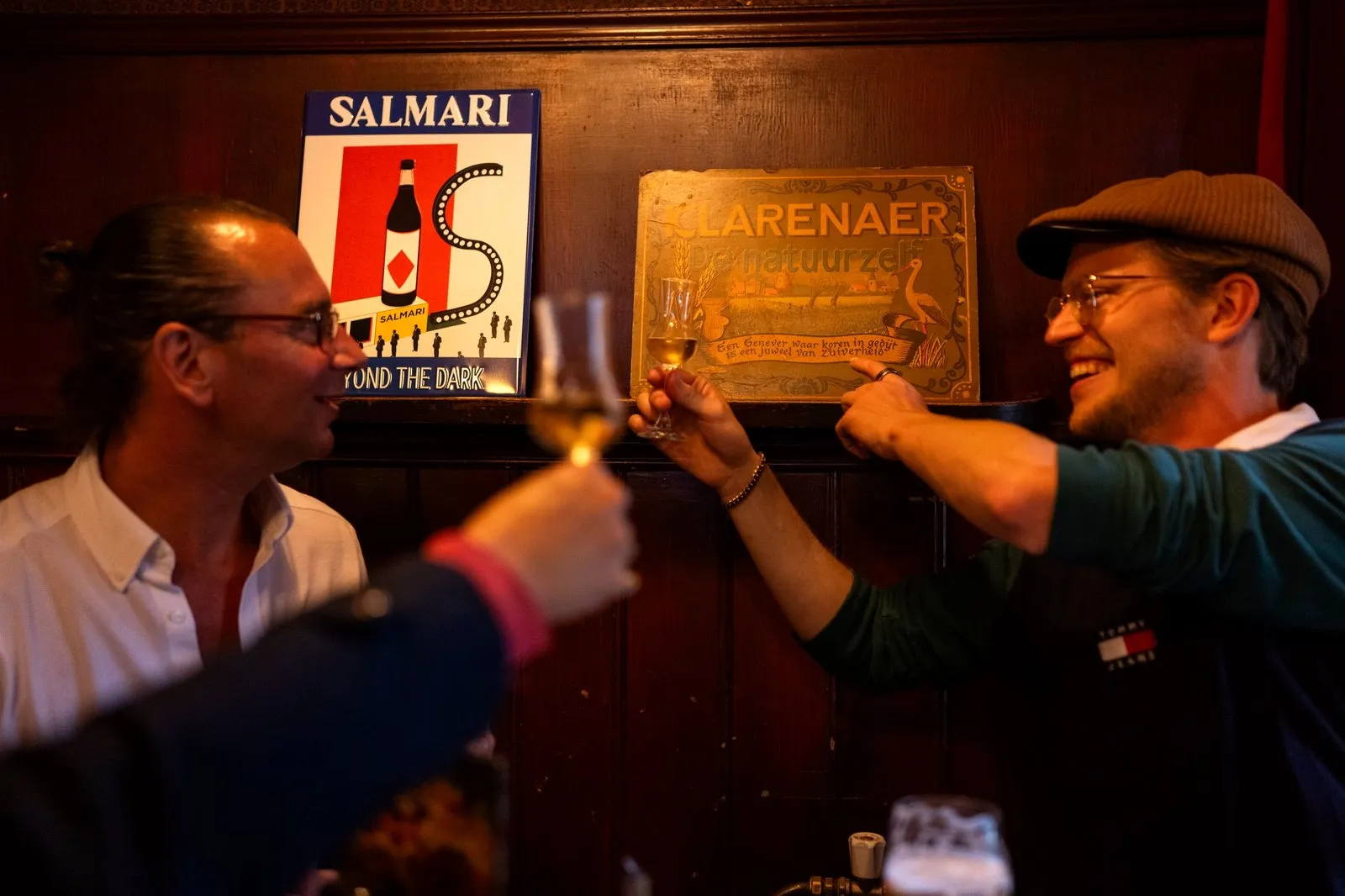 Two men toasting small glasses of jenever in an Amsterdam brown cafe