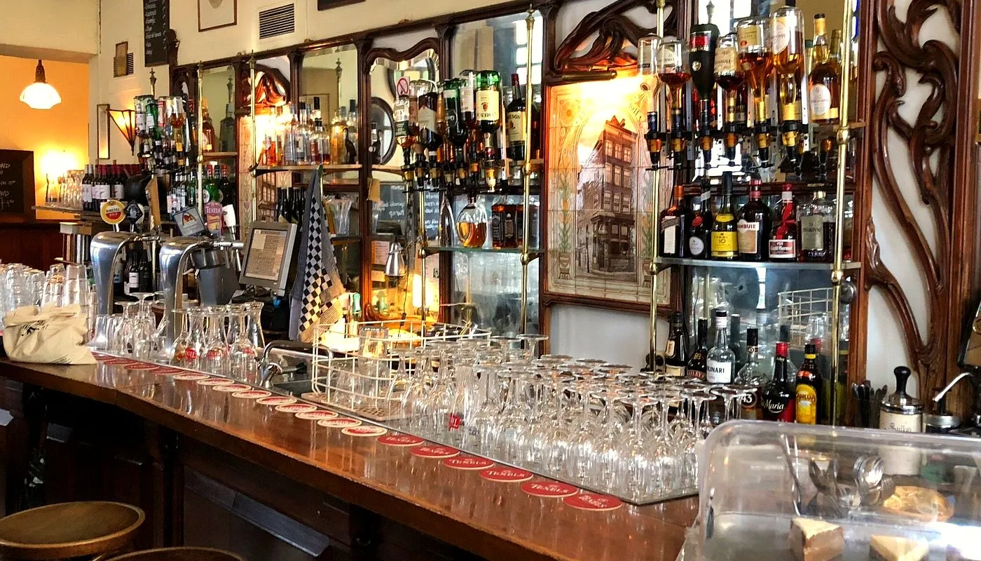 Classic Amsterdam cafe bar with rows of polished wine glasses on the wooden counter, mirrored shelves of liquor bottles and art nouveau woodwork