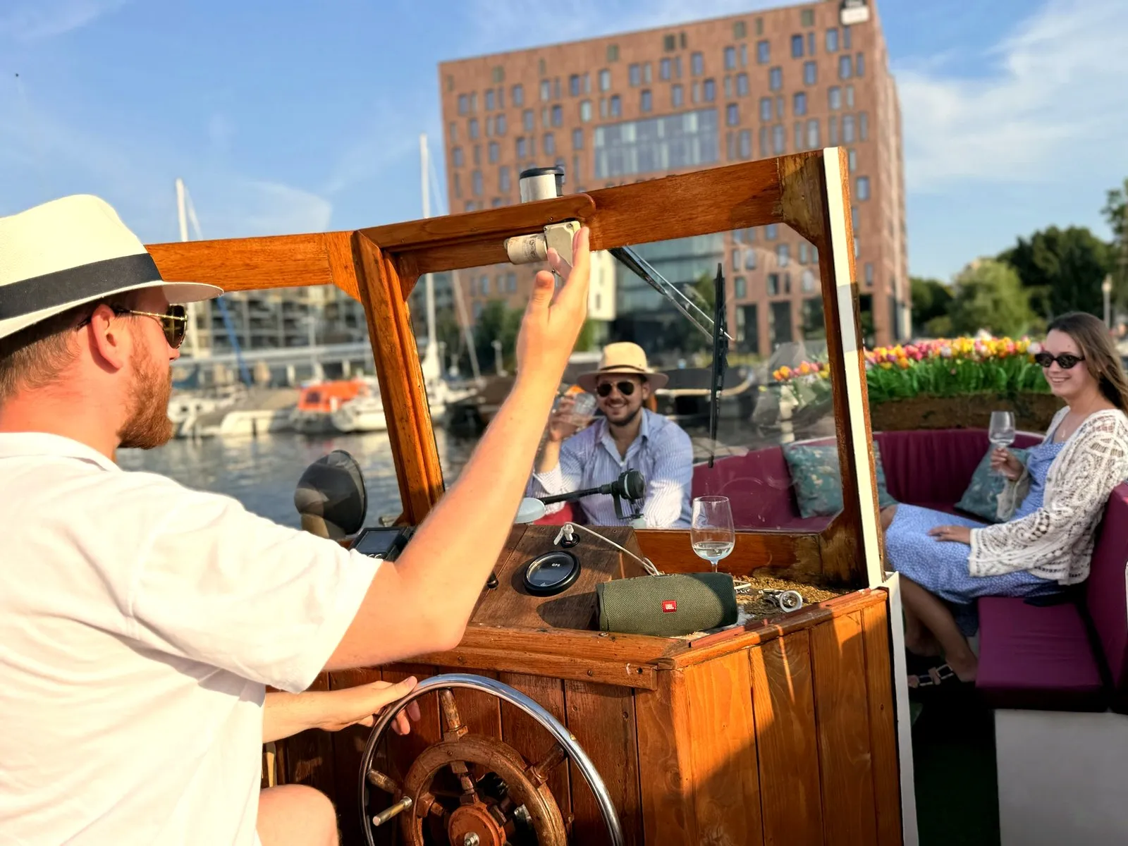 The captain steering an Amsterdam salon boat while guests relax with drinks and tulips beside them