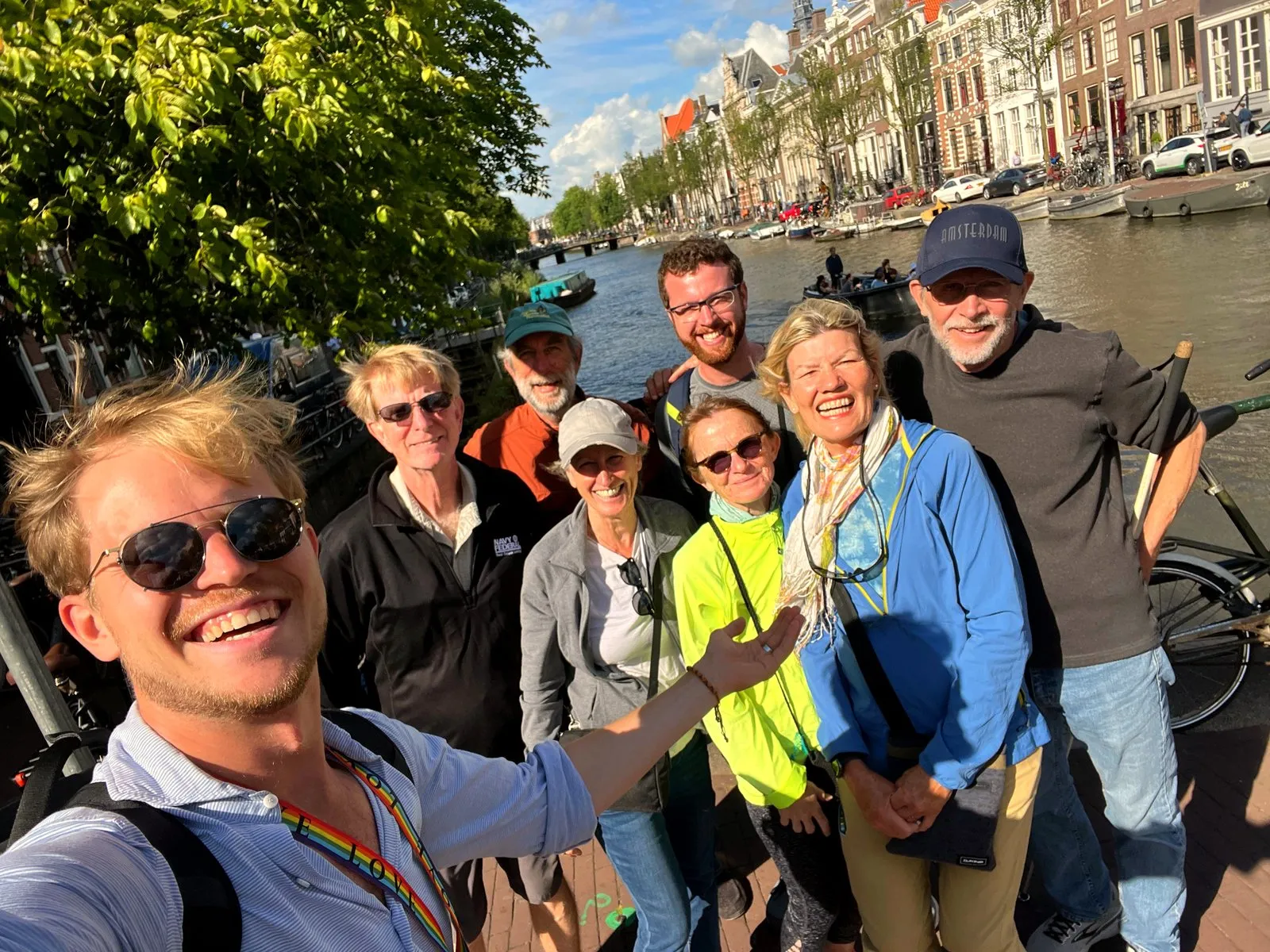 A guide and a group of guests smiling for a selfie on a sunny Amsterdam canal bridge