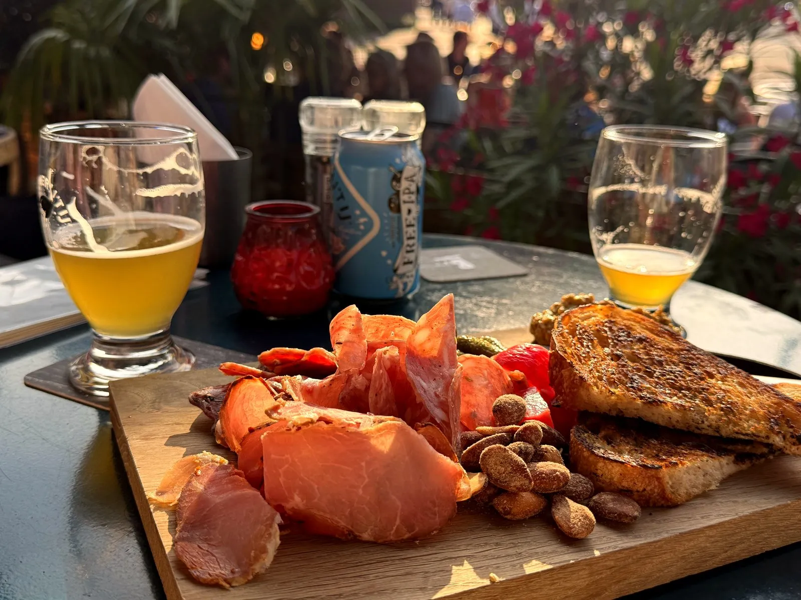 Wooden board of cured ham, nuts and grilled bread with two beers on a terrace table at golden hour