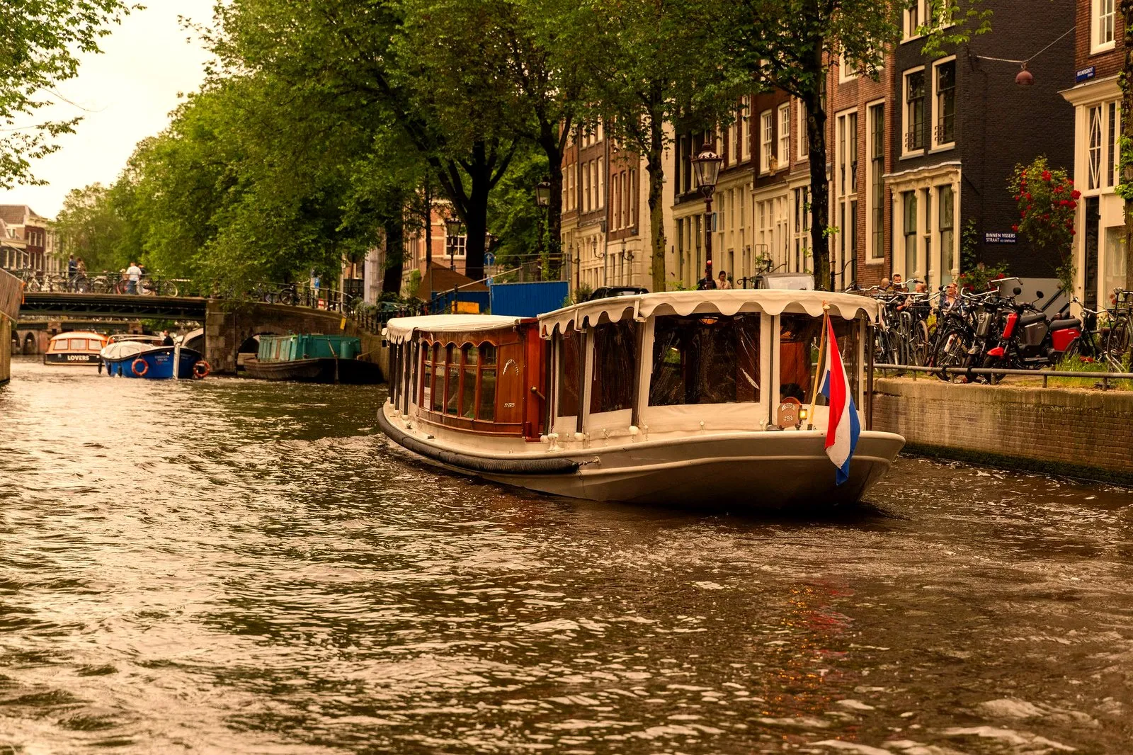 A classic Amsterdam salon boat with a roof cruising a city canal