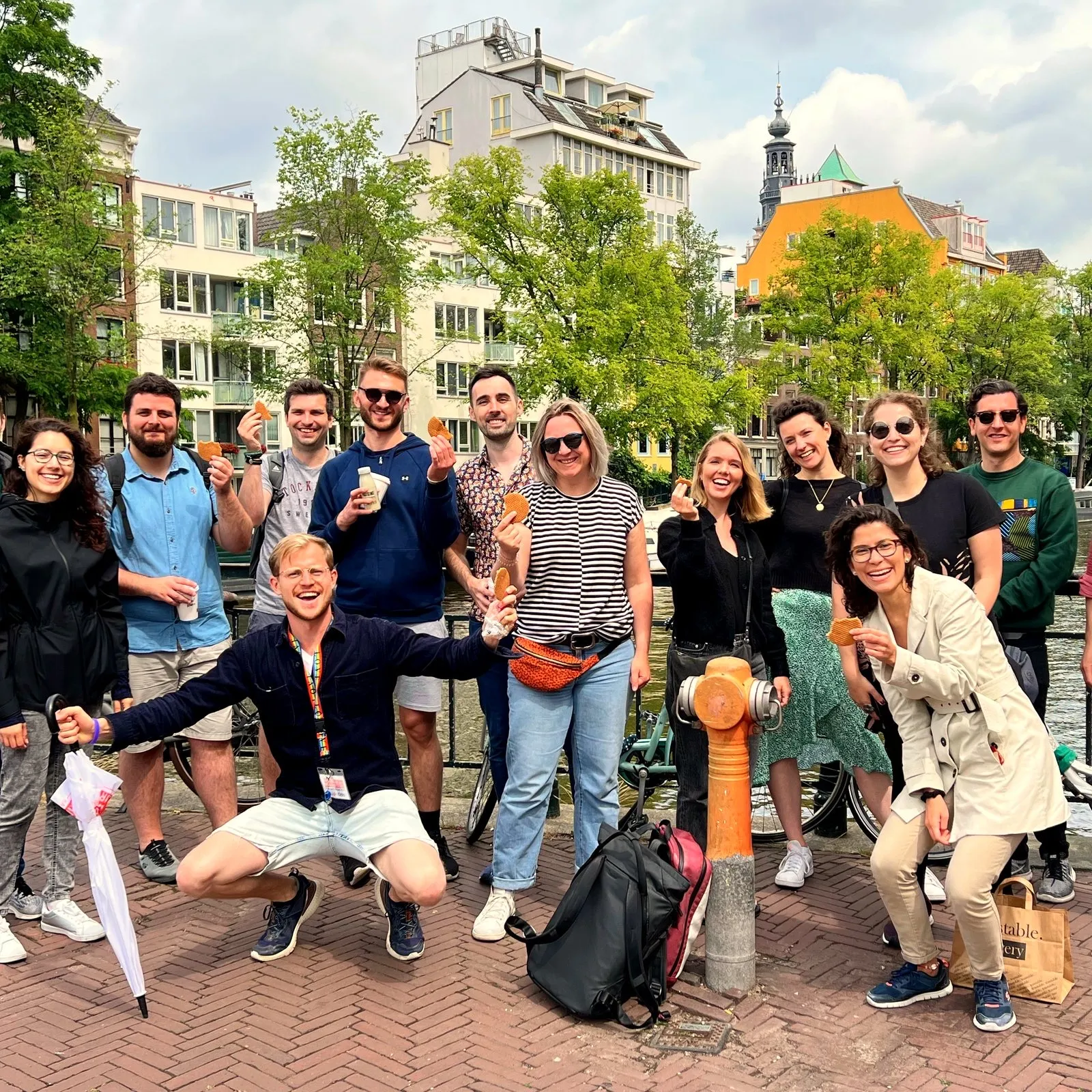 A team of twelve throw their arms up and cheer with stroopwafels on an Amsterdam canal bridge, their guide kneeling in front
