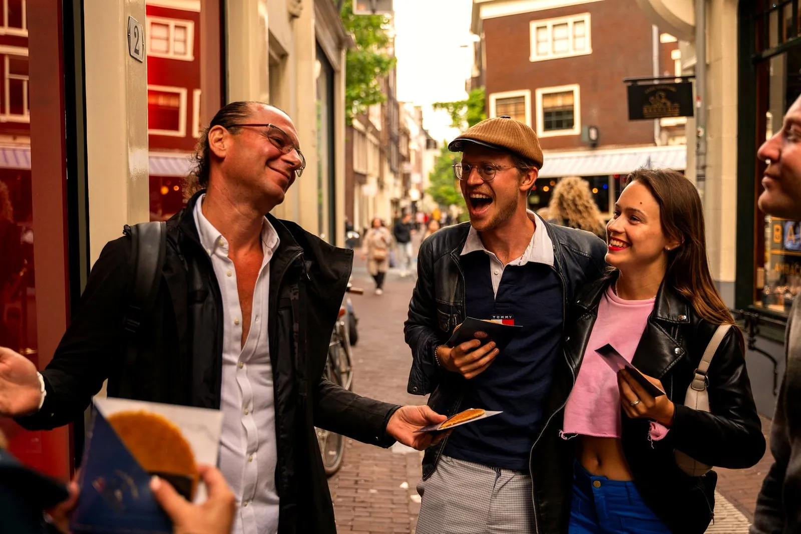 A guide handing a stroopwafel to two laughing guests on an Amsterdam street