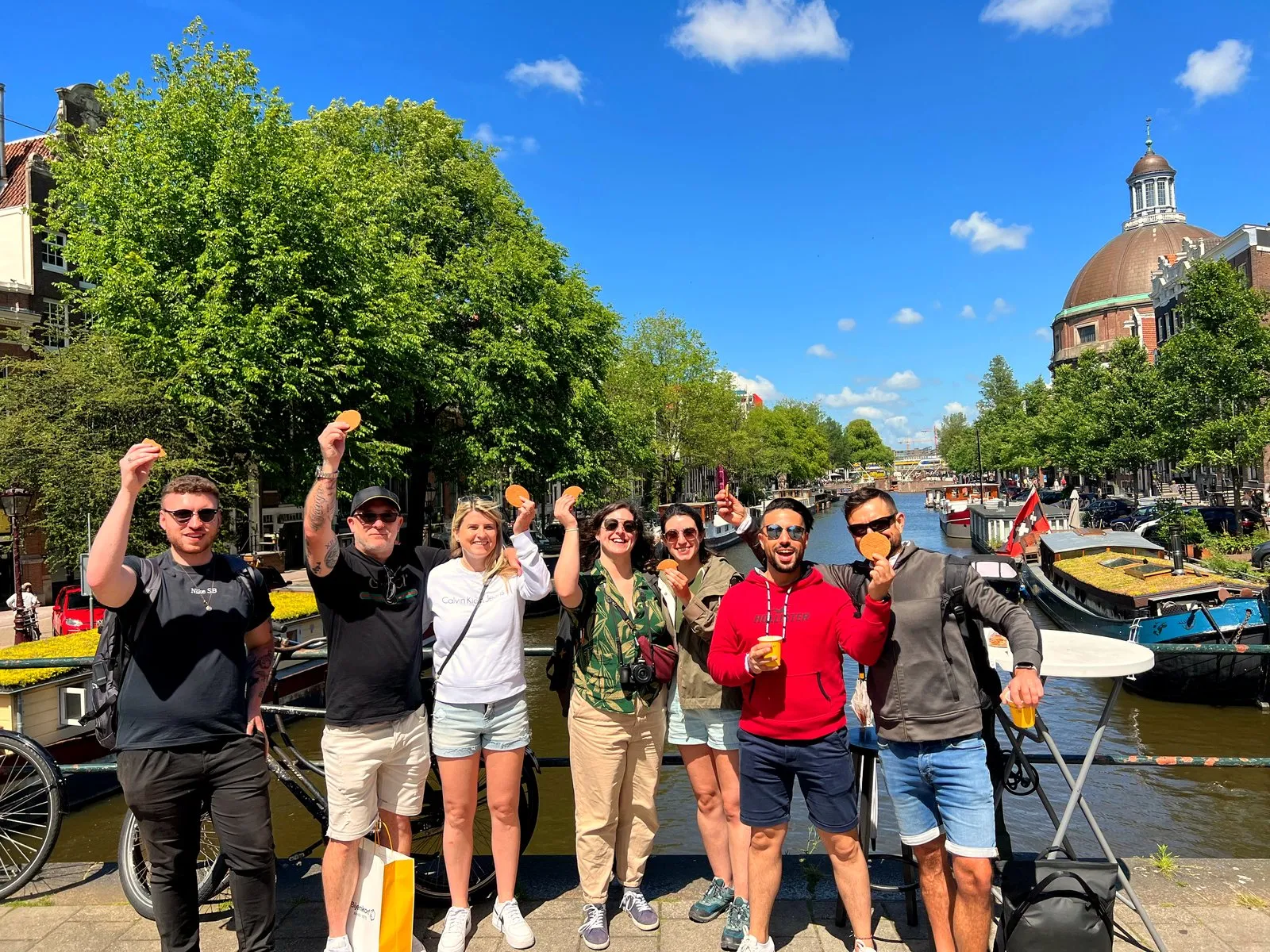 A group holding up stroopwafels on a sunny Amsterdam canal bridge