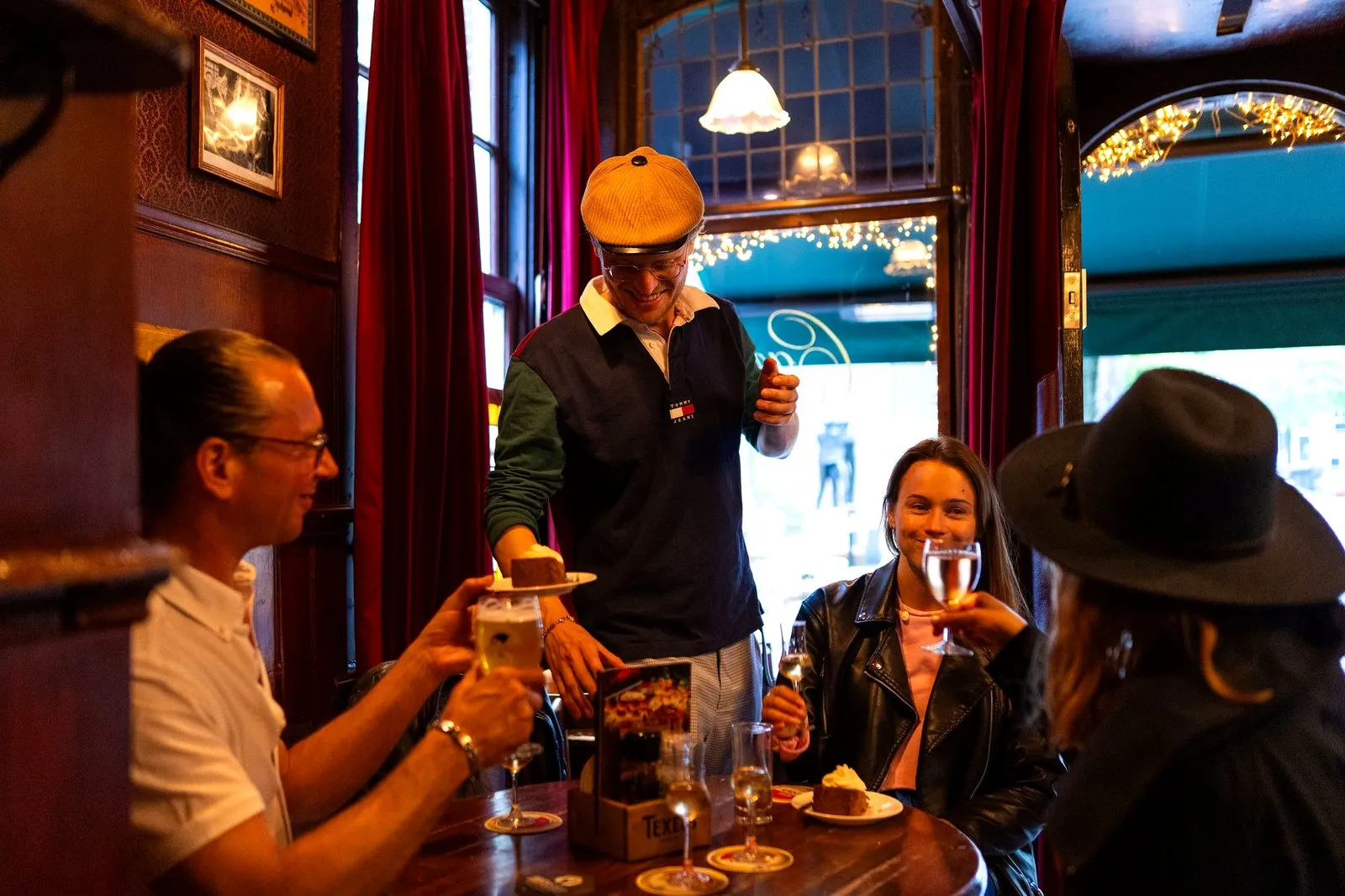 A guide serving cake to seated guests in a warm Amsterdam brown bar