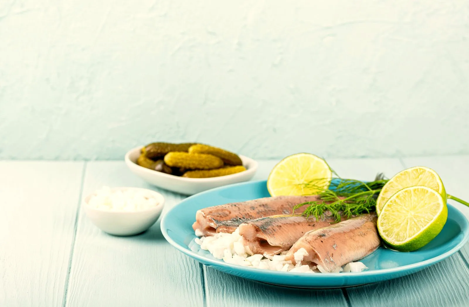 Dutch herring fillets on a blue plate with lime, dill and pickles
