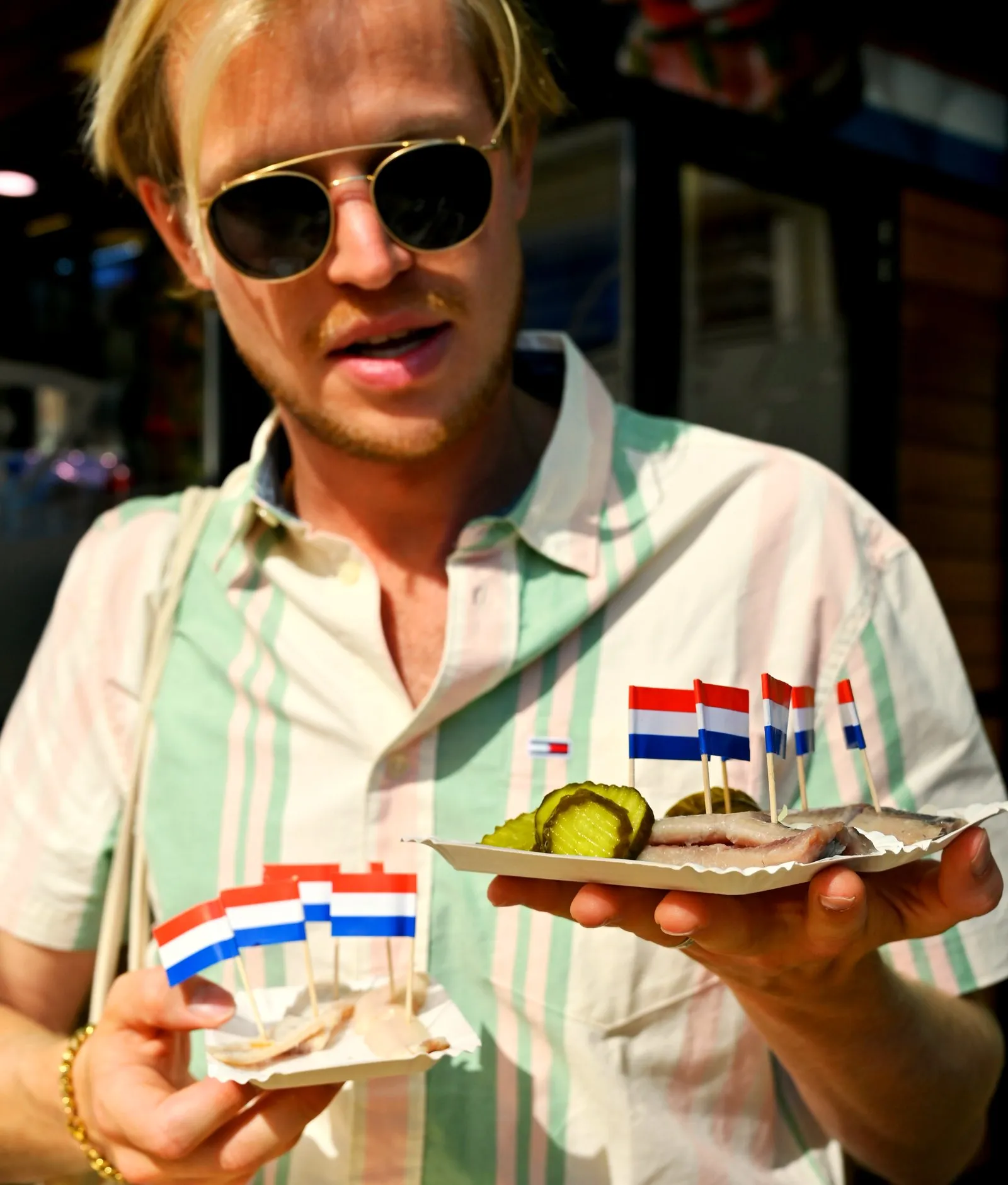 A guest holding two trays of raw herring with pickles and small Dutch flags on the food tour