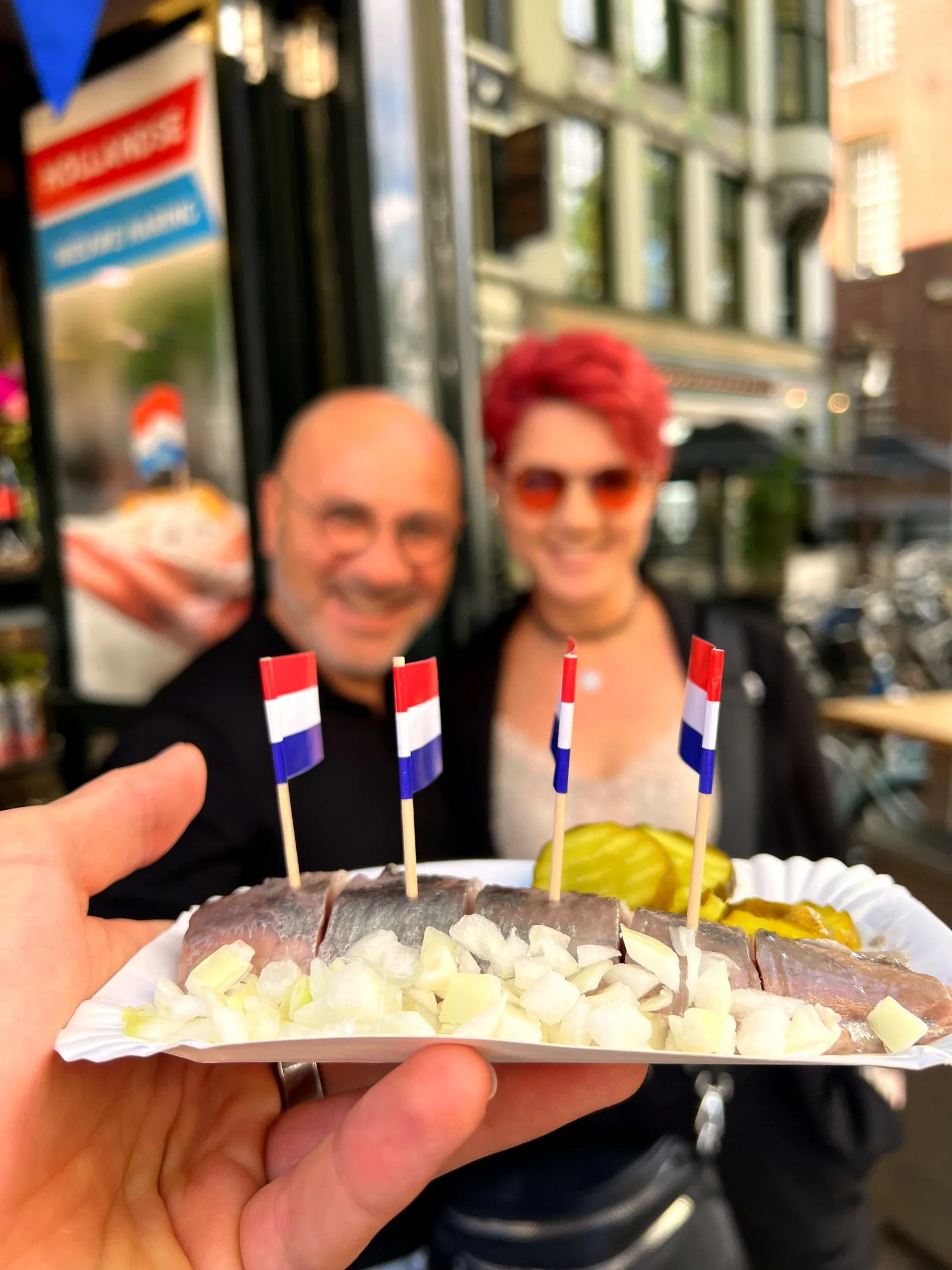 Close-up of a herring tray with chopped onion and Dutch flag picks held up in front of a couple