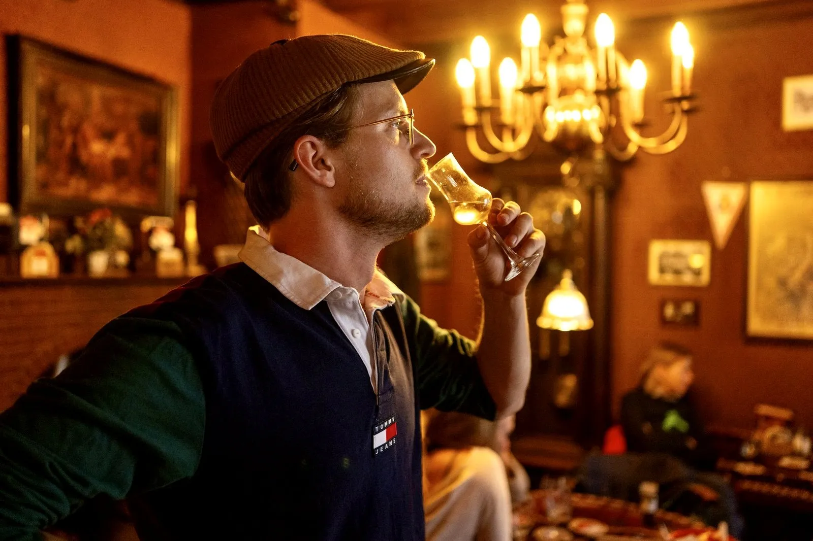 A guest sipping jenever from a tulip glass in a candlelit Amsterdam brown bar