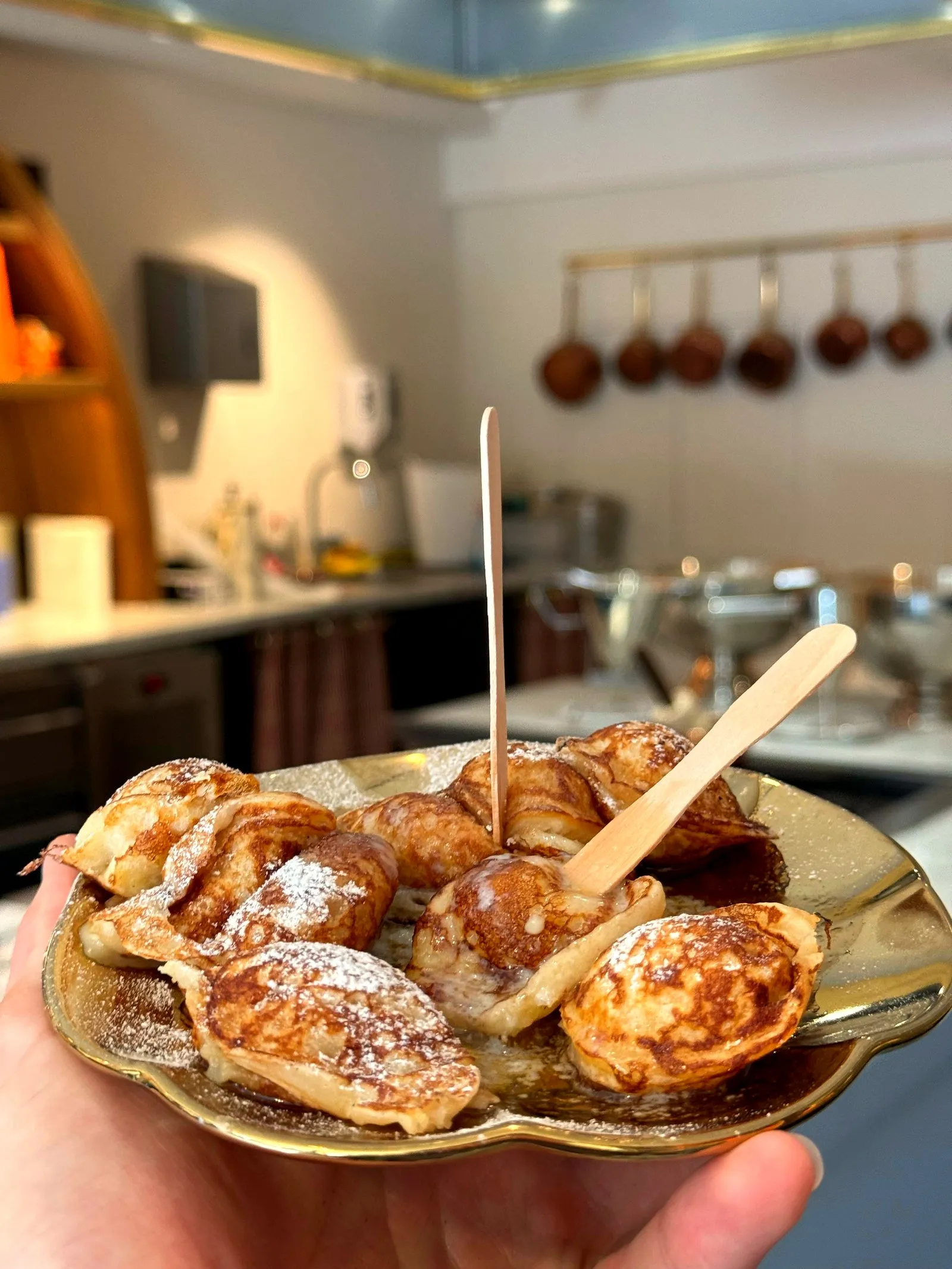Hand holding a brass plate of poffertjes dusted with powdered sugar