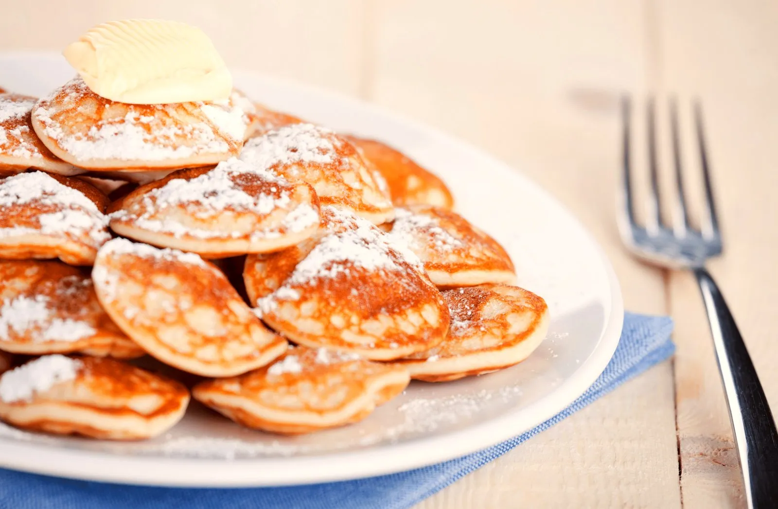 Plate of mini Dutch poffertjes pancakes topped with powdered sugar and butter