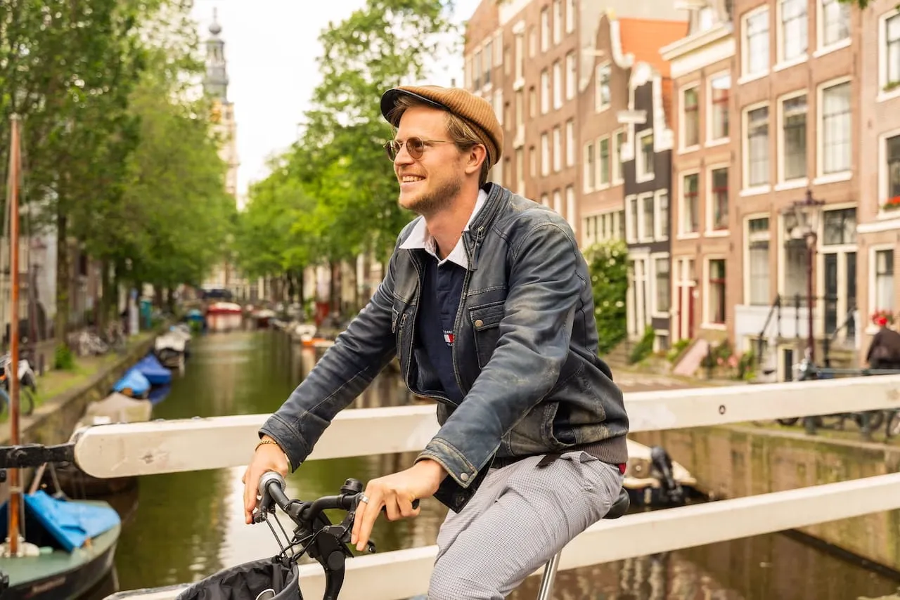 A smiling guide on a bike on an Amsterdam canal bridge with the Zuiderkerk tower behind