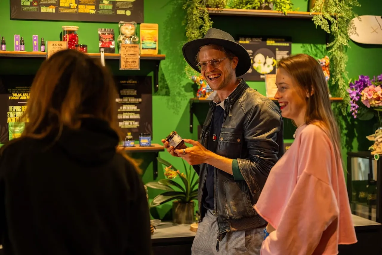 A guide showing a product to two guests in a bright green Amsterdam coffeeshop