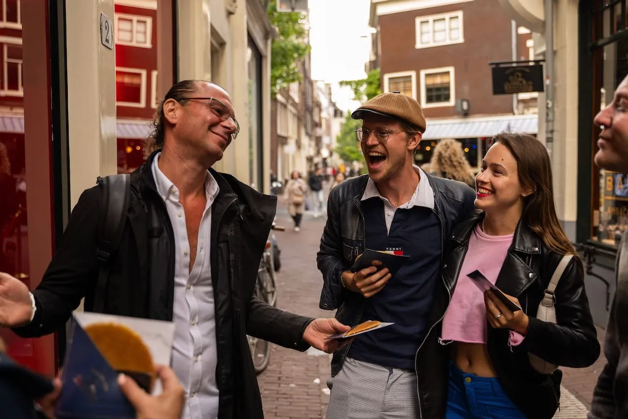 A guide handing a stroopwafel to laughing guests in a Red Light District alley