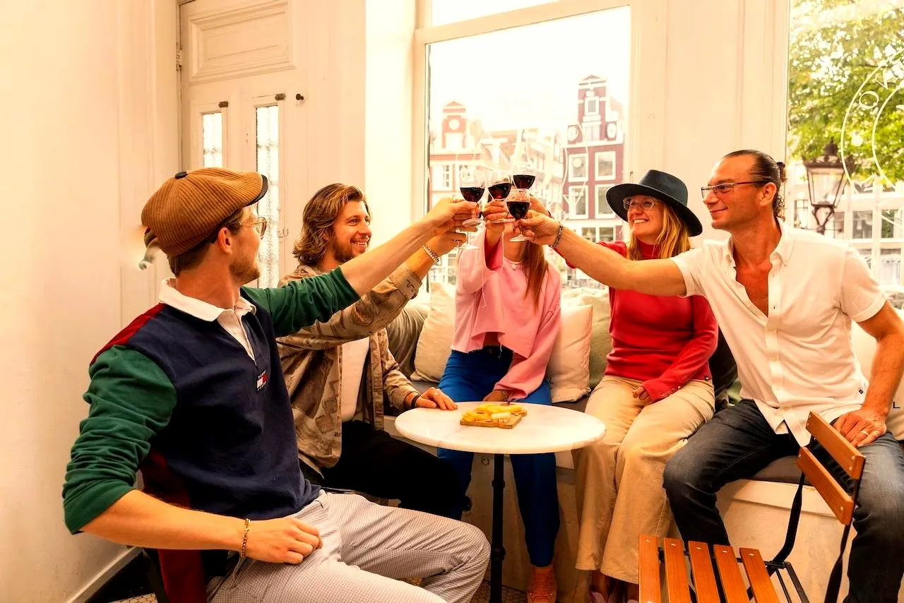Five guests toasting wine glasses in a bright room overlooking canal houses
