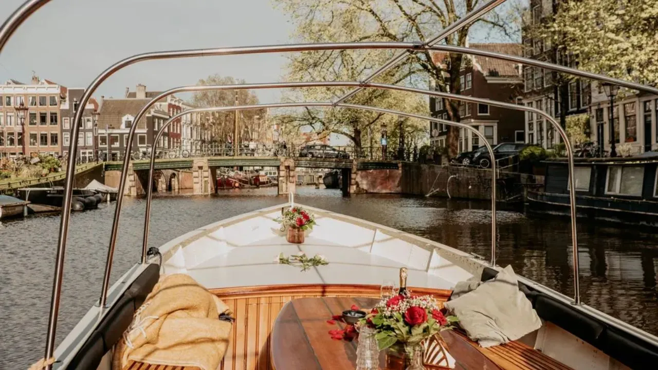 Canal boat tour in Amsterdam passing under bridges with historic canal houses and tree-lined streets