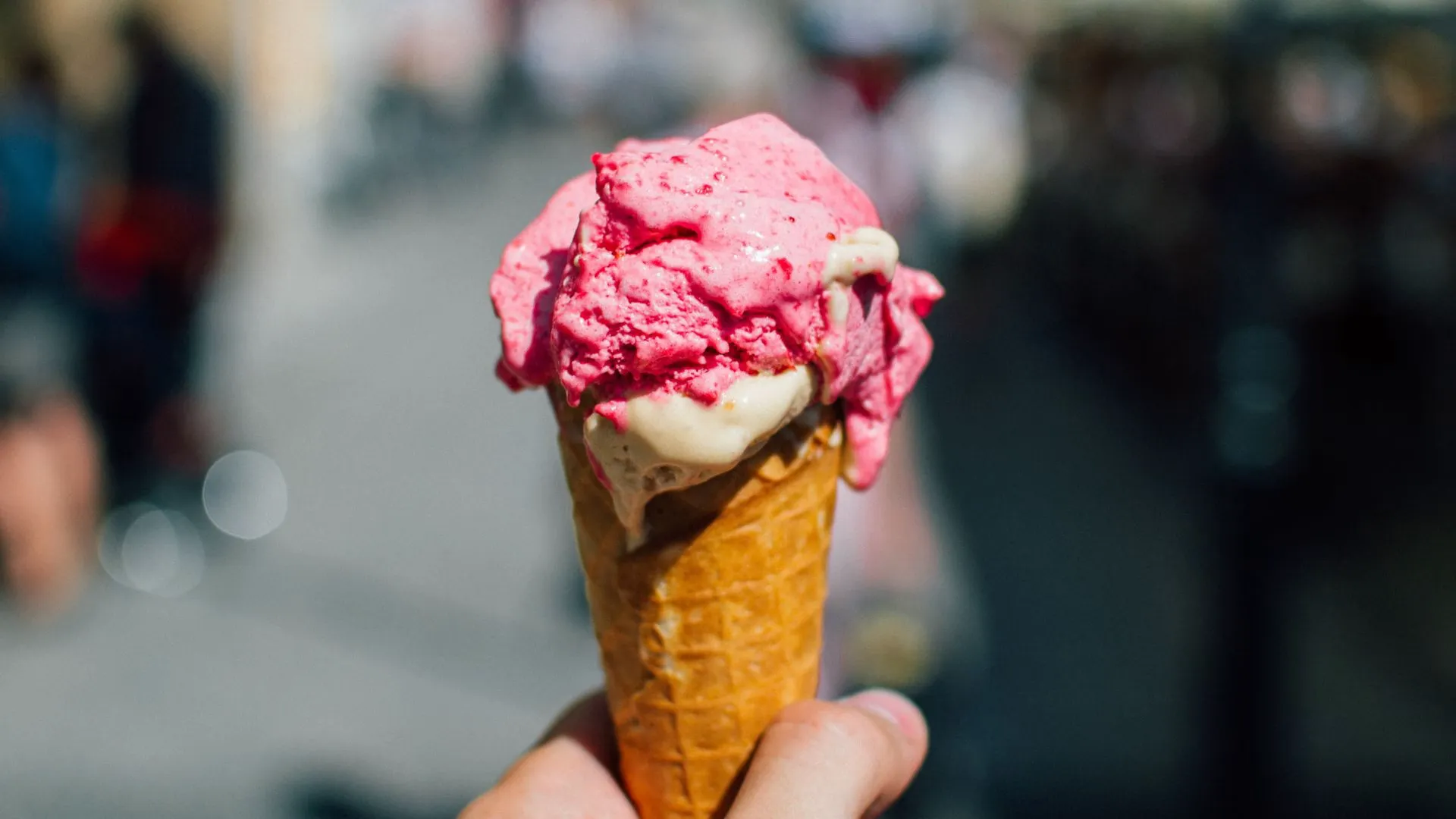 Hand holding a waffle cone with melting raspberry and vanilla ice cream on a sunny street