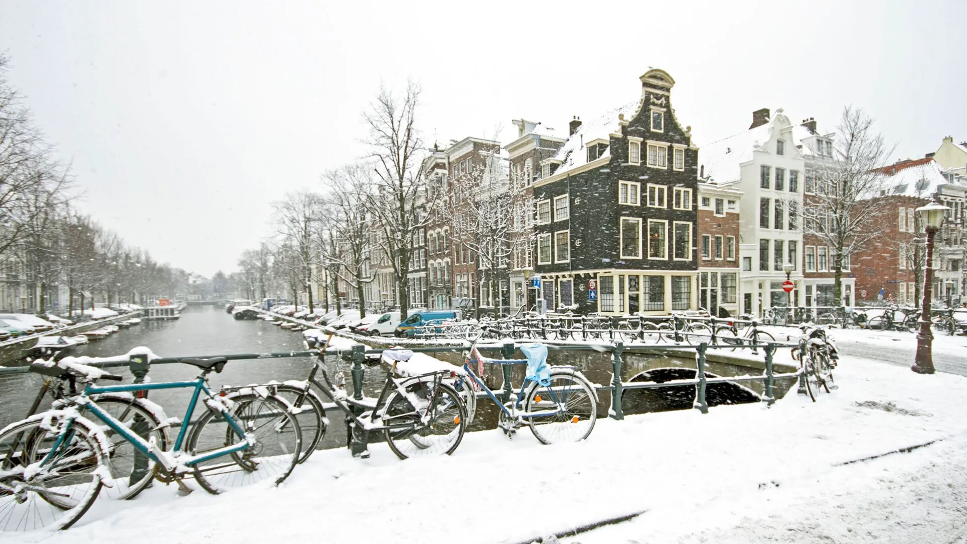 Amsterdam canal in heavy snow with bicycles lined along a white bridge and snow-dusted gabled houses