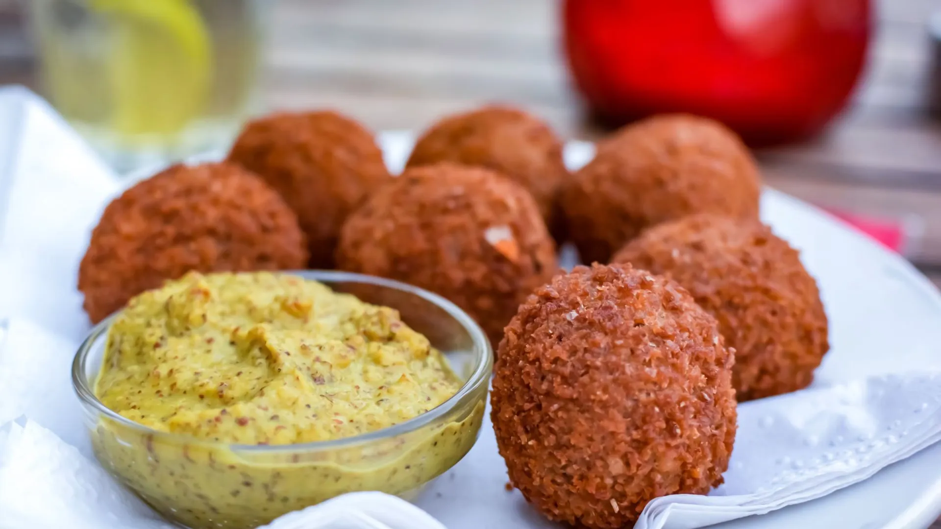 Close-up of crispy golden-brown bitterballen on a plate next to a small glass bowl of coarse mustard