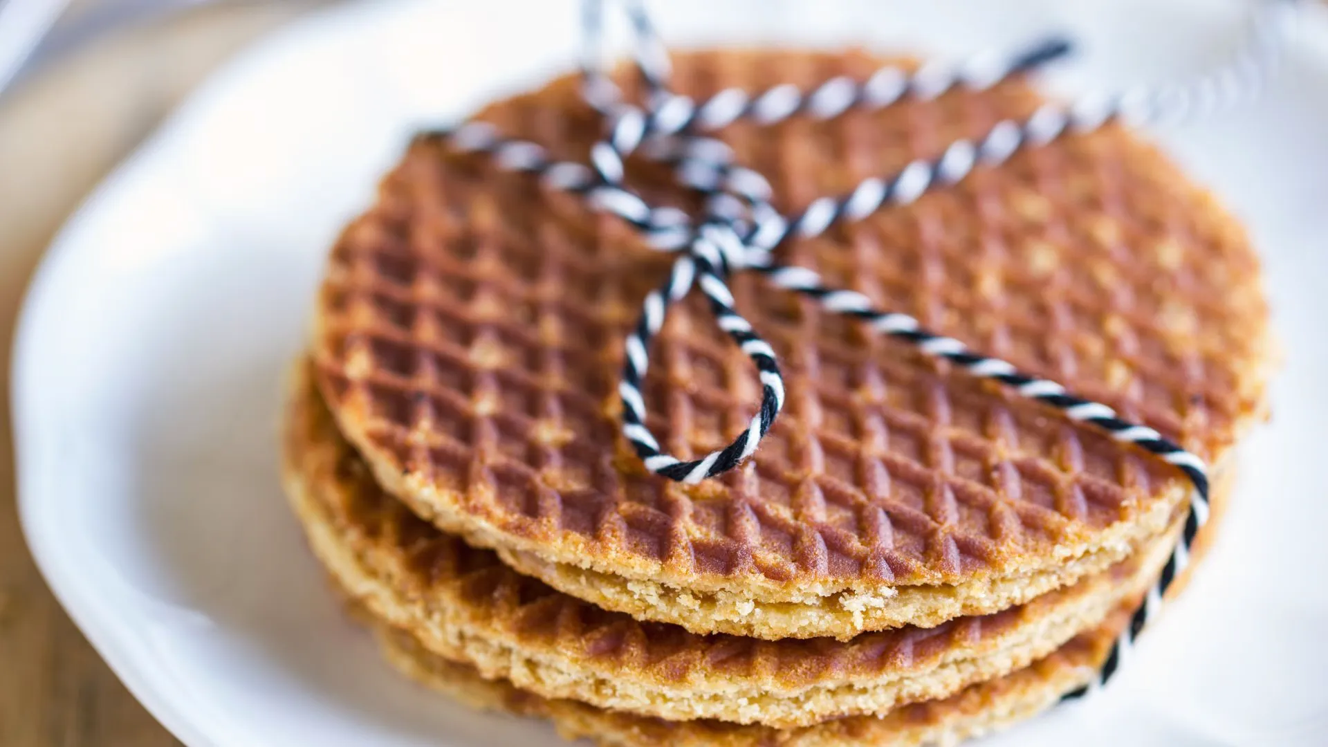 Stack of three stroopwafels tied with black and white striped twine on a white plate