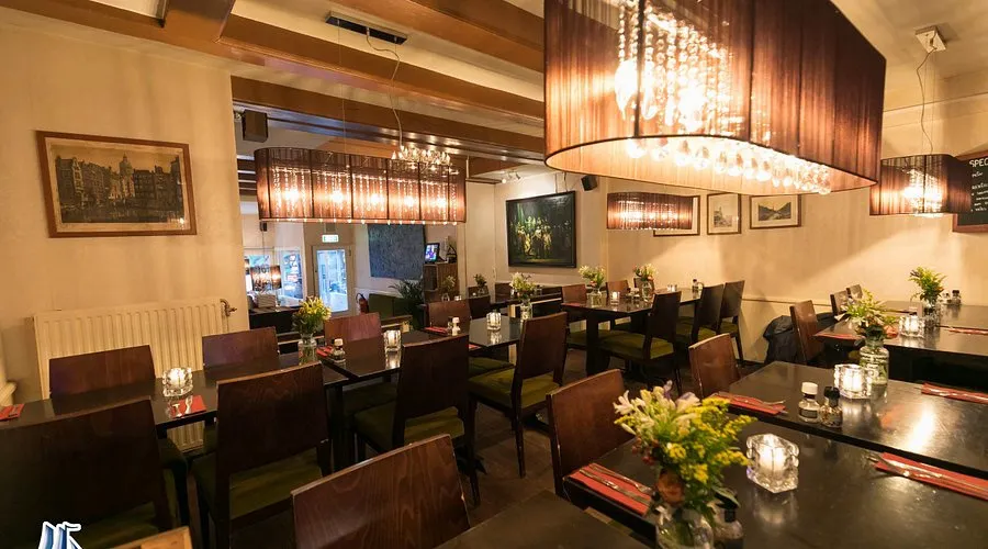 Cozy restaurant dining room with dark wooden tables, green cushioned chairs, fresh flowers and warm drum chandeliers