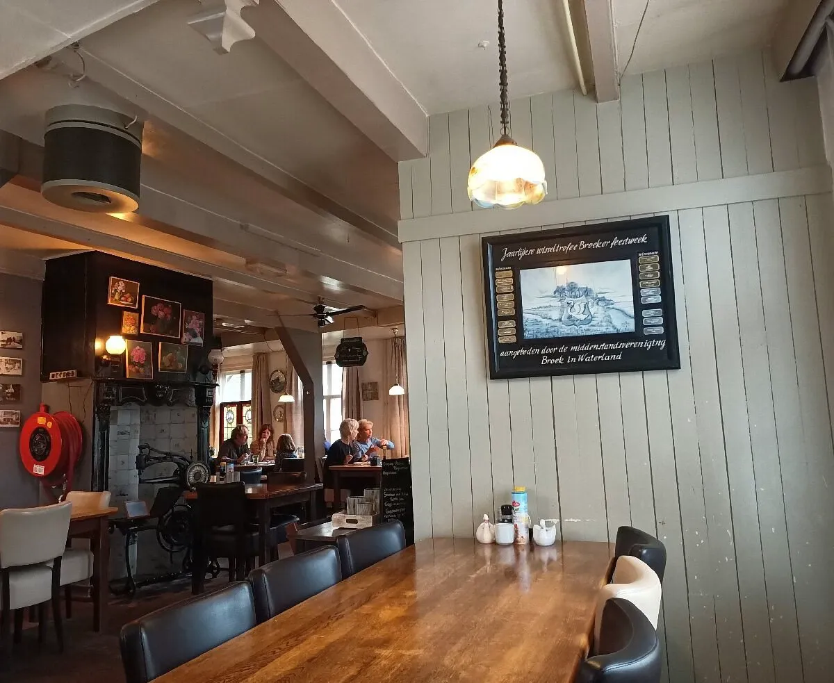 Rustic Dutch country restaurant interior with wood panelled walls, a long wooden table and diners near an old fireplace