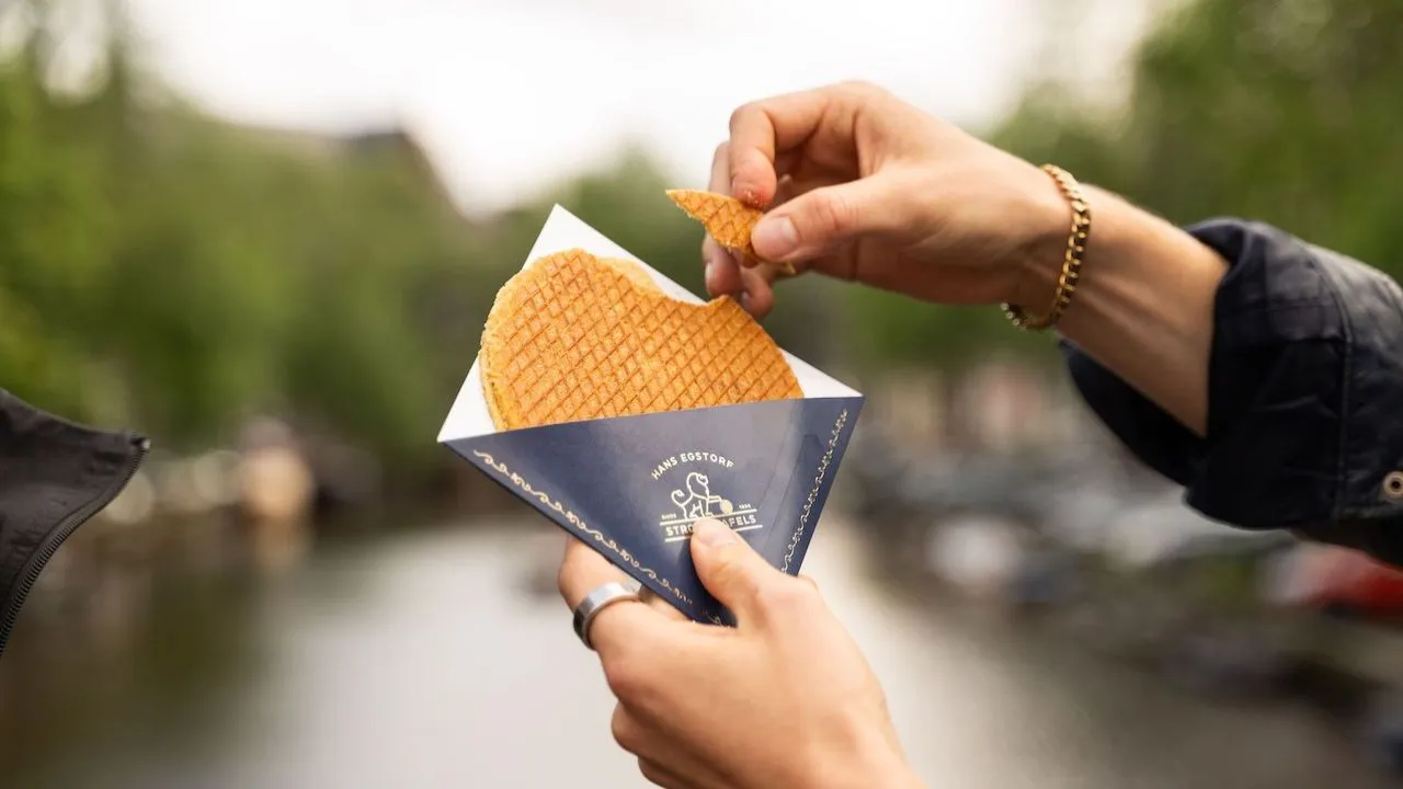 Fresh Dutch stroopwafel held in a paper sleeve over an Amsterdam canal
