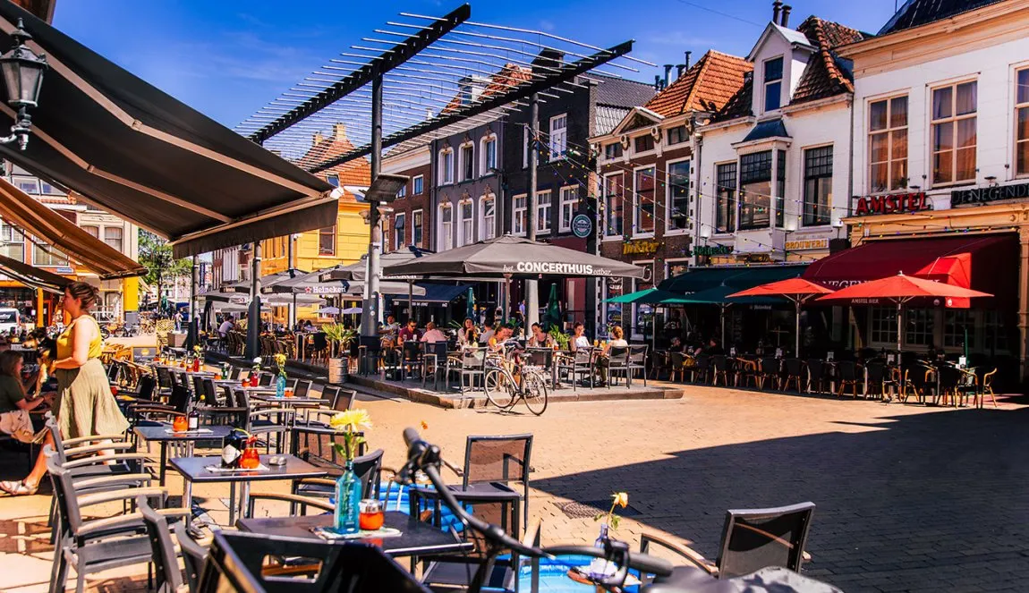 Sunny Dutch city square in Groningen lined with cafe terraces, parasols, and historic gabled buildings