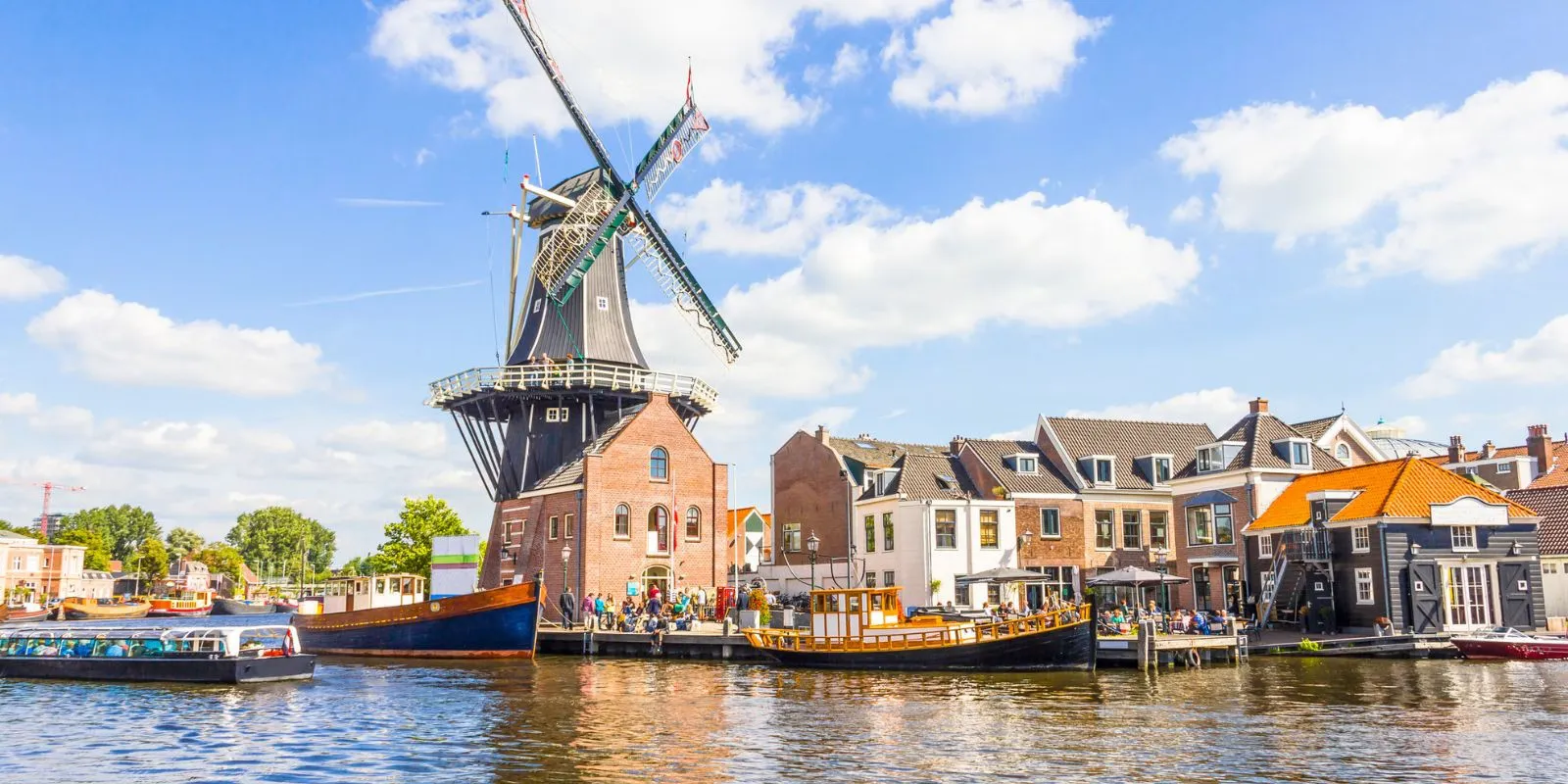 The De Adriaan windmill and old boats on the Spaarne river in Haarlem under a blue sky