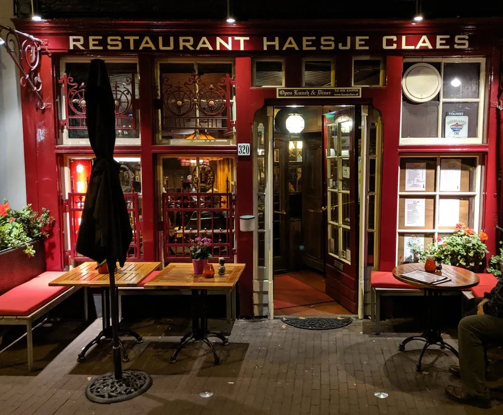 Red facade of Restaurant Haesje Claes in Amsterdam at night with wooden terrace tables and flower boxes