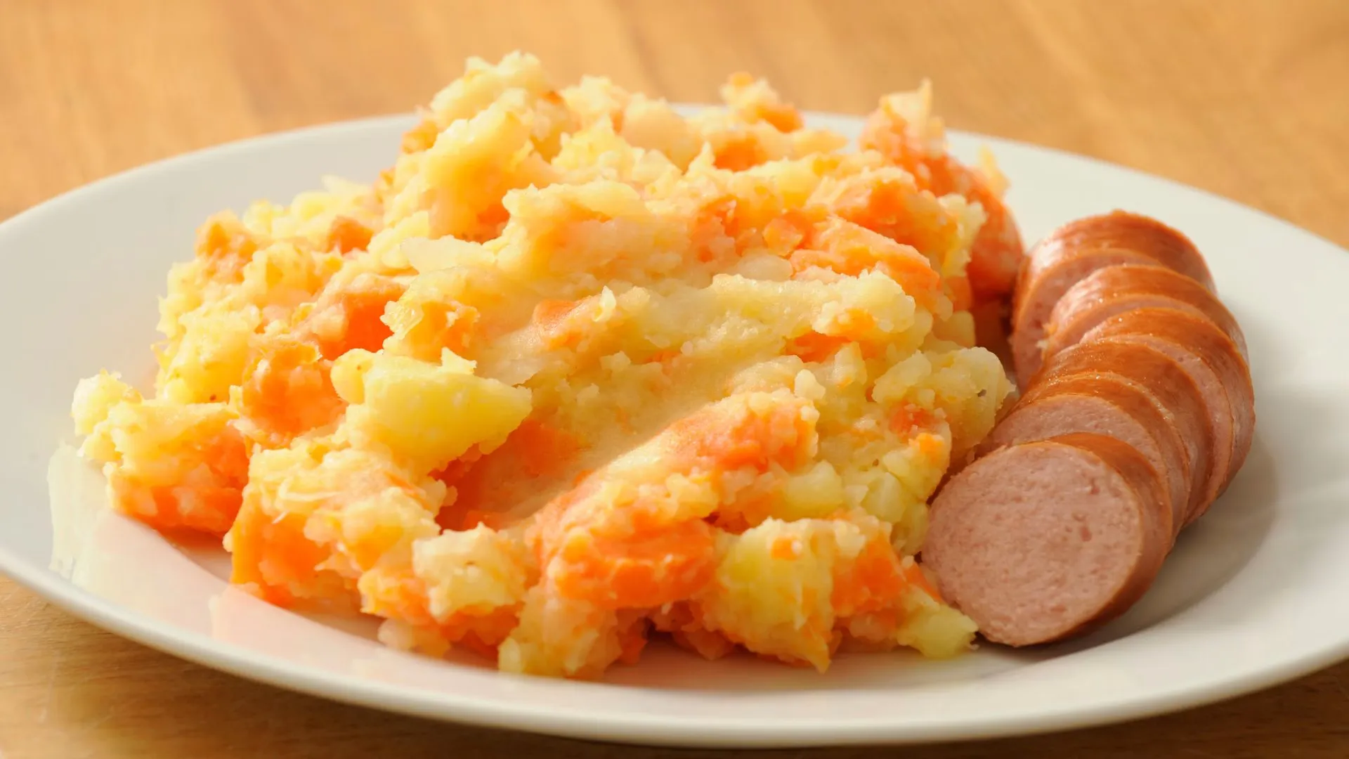 Plate of hutspot, mashed potatoes with carrot and onion, served with slices of smoked rookworst sausage