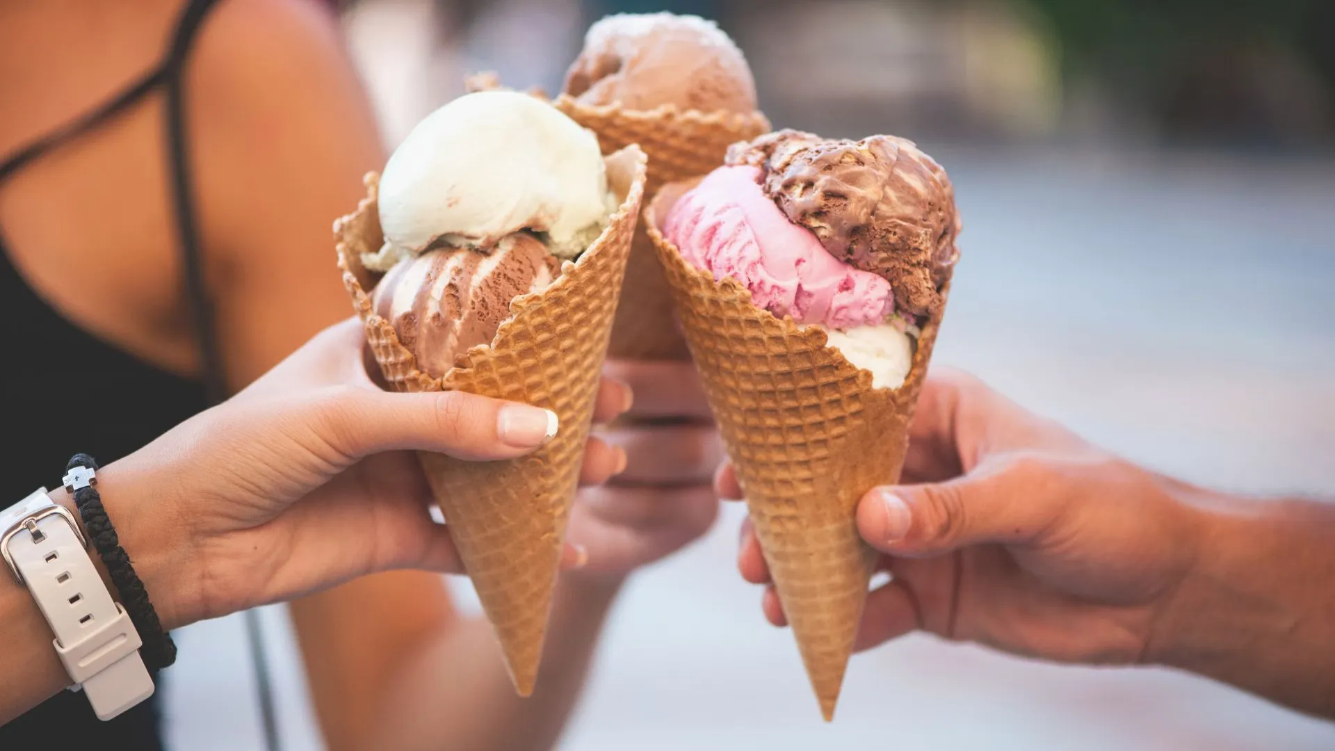 Three hands holding waffle cones stacked with chocolate, vanilla and strawberry ice cream