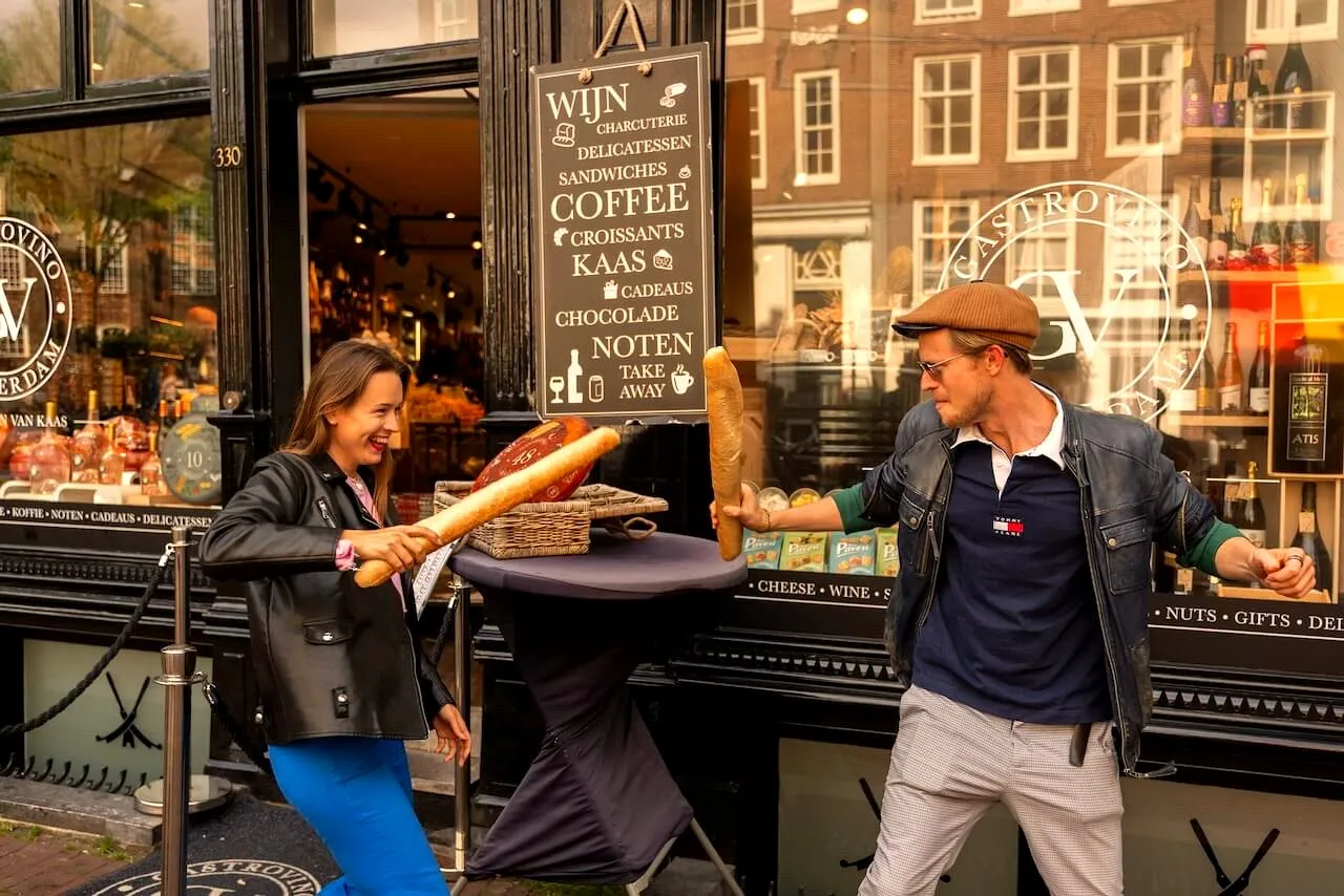 Playful owners of Adam & Eve Tours having a baguette sword fight outside an Amsterdam deli