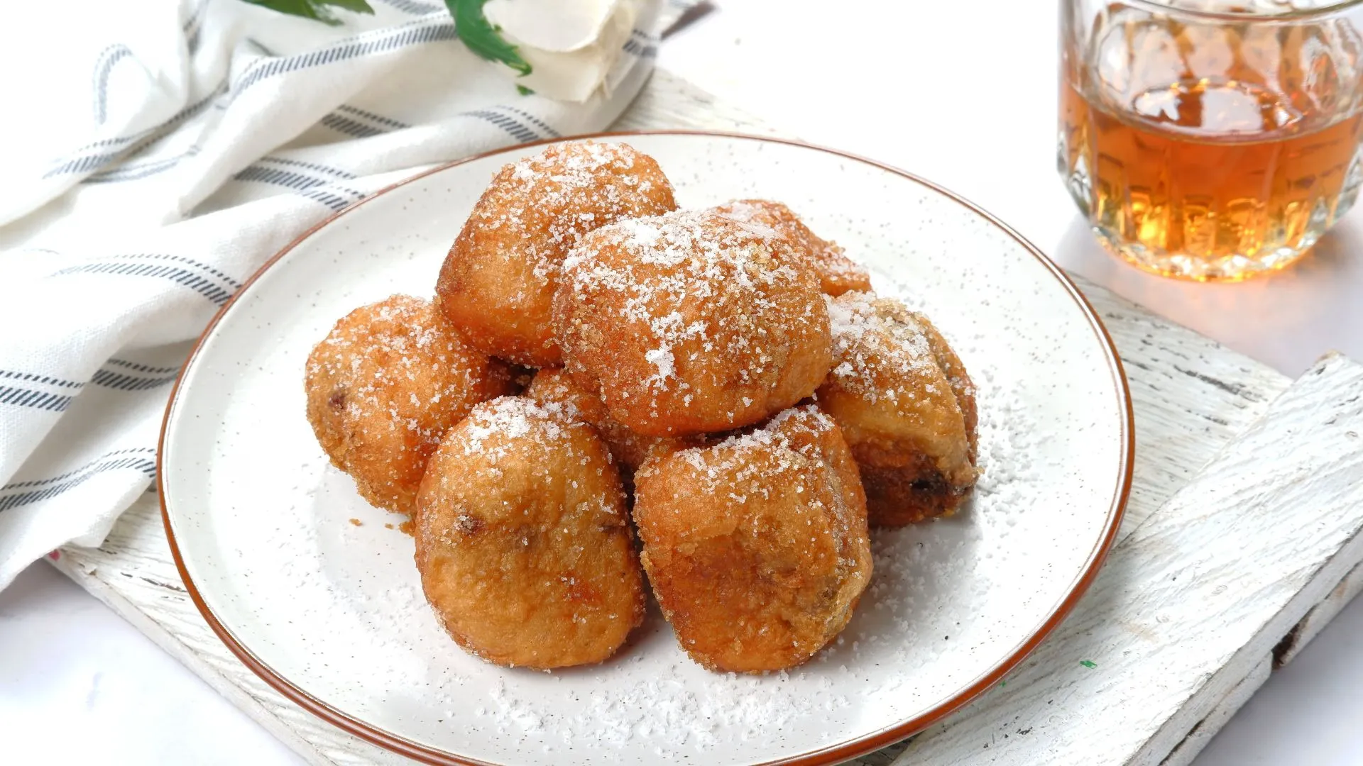 Plate piled with oliebollen, Dutch fried dough balls dusted with powdered sugar, with a glass of amber drink behind