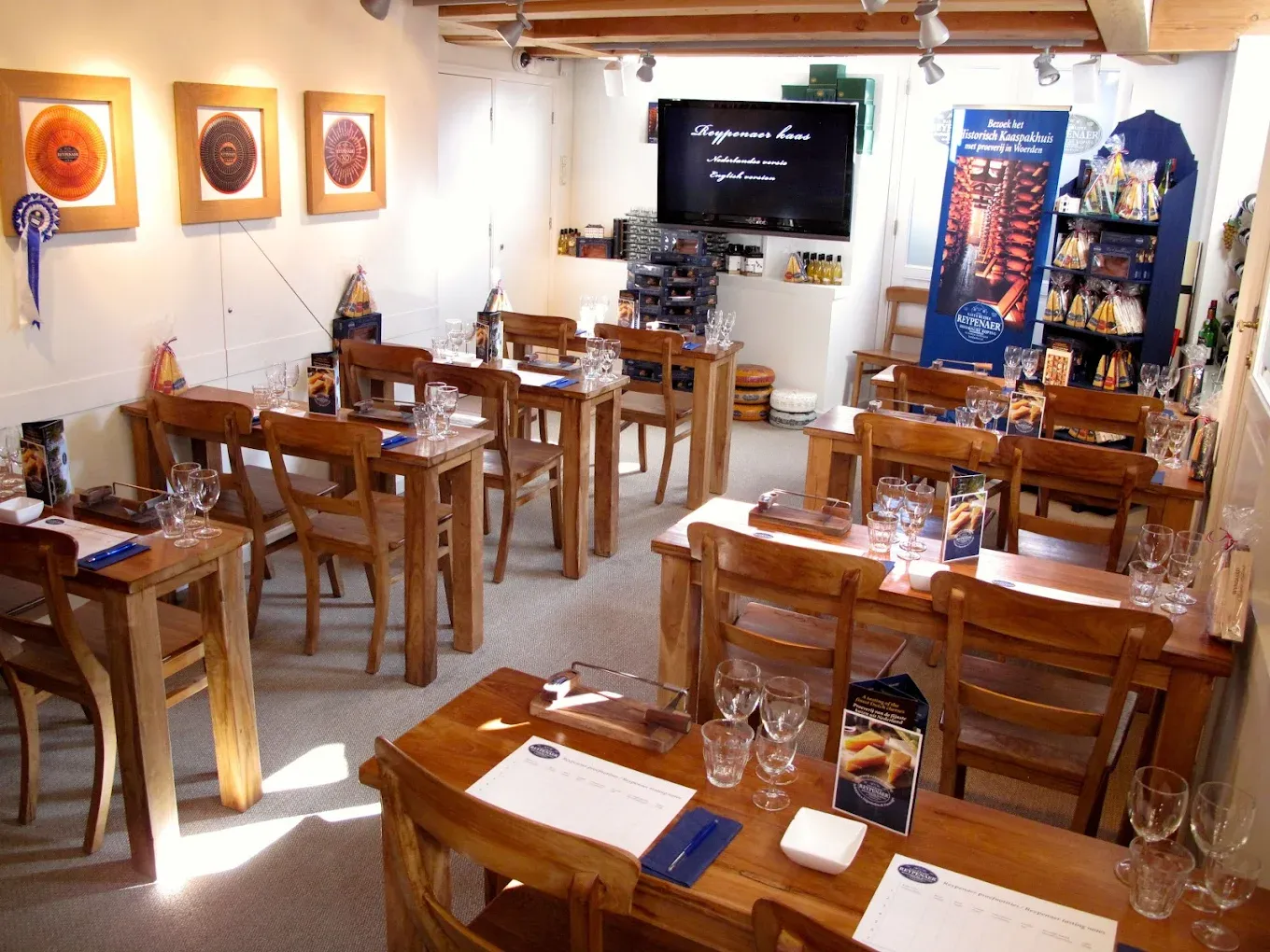 Tasting room with rows of wooden desks set with wine glasses, cutting boards and scorecards, framed cheese wheels on the wall