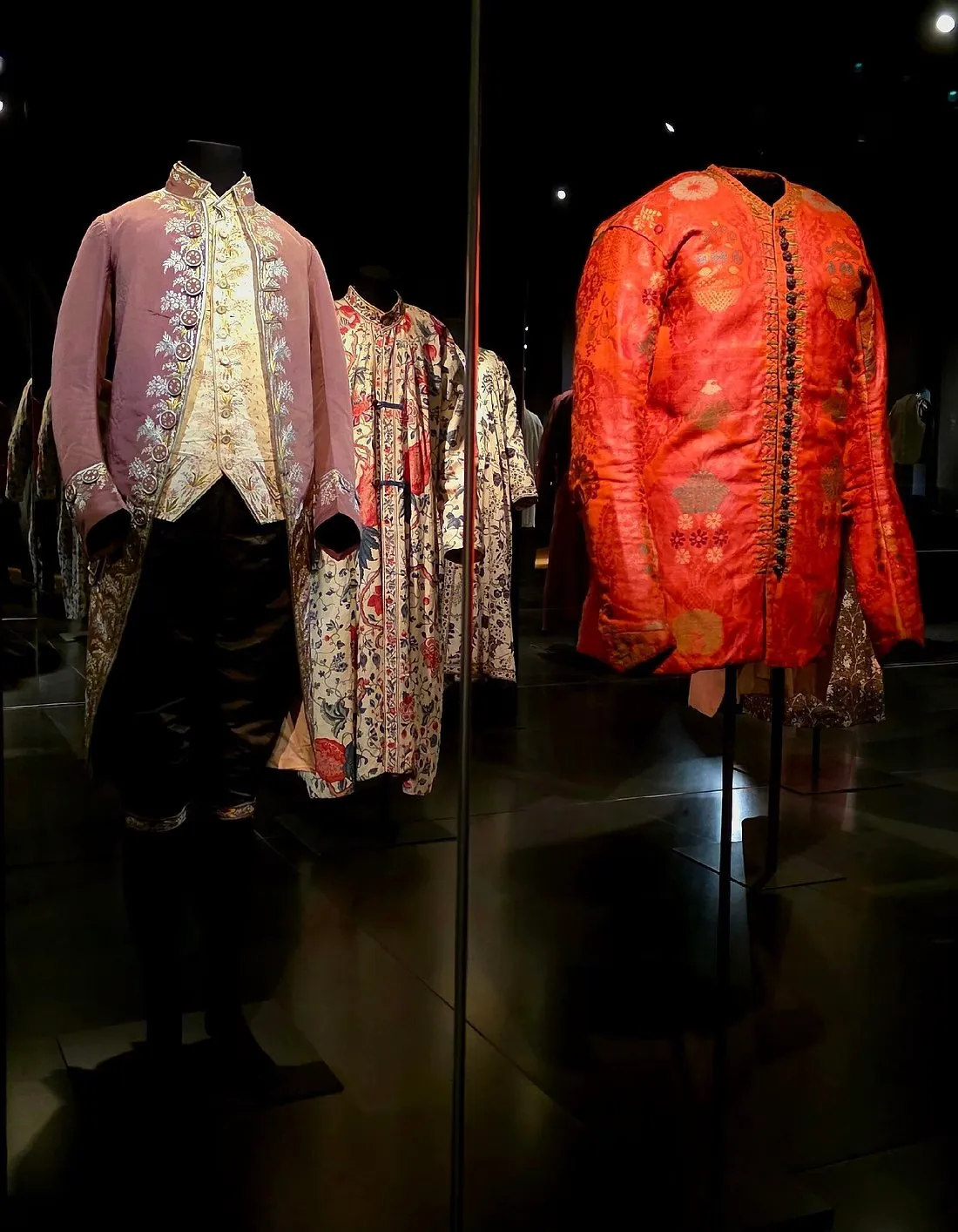 Eighteenth-century men's coats and embroidered waistcoats displayed on mannequins in a dark museum gallery