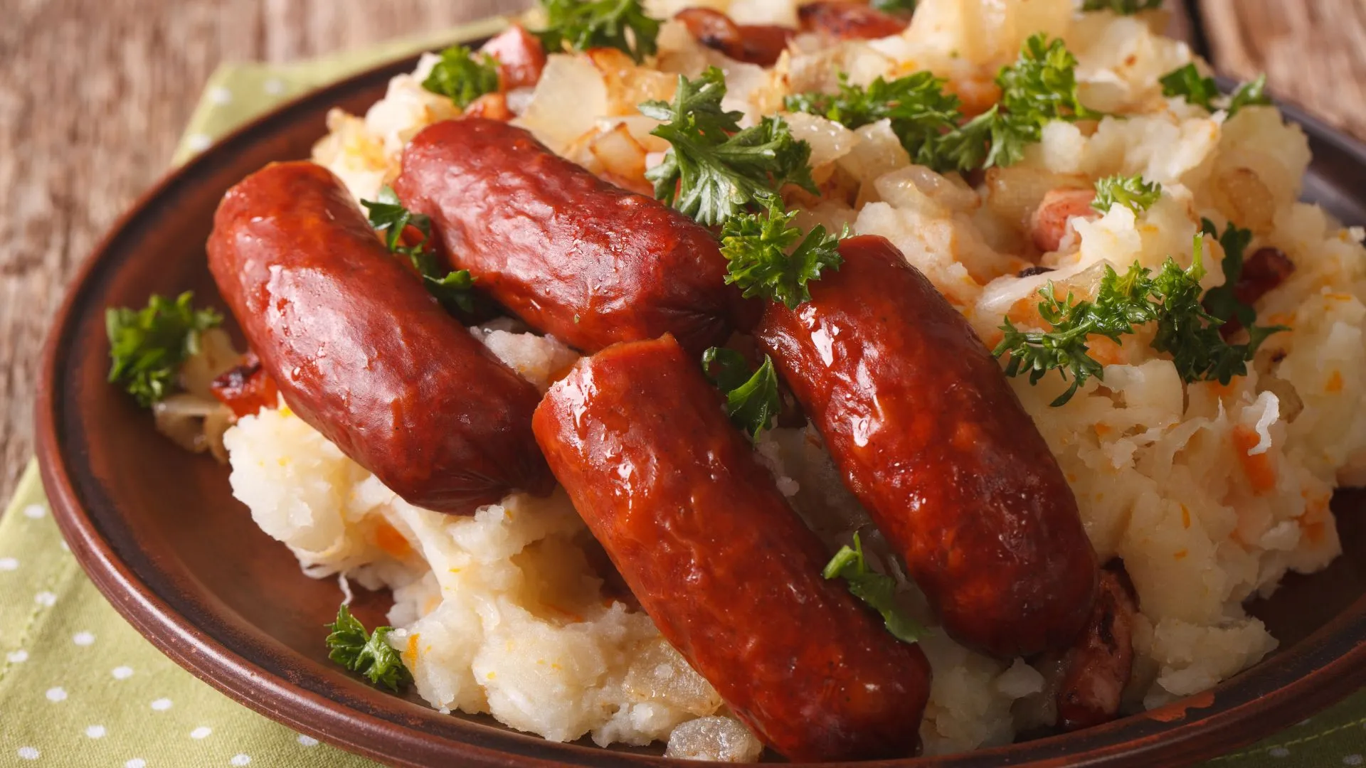 Plate of mashed potato stamppot topped with small smoked sausages and fresh parsley