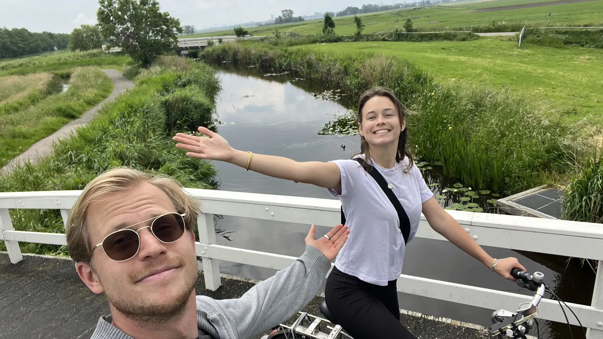Adam & Eve Tours founders Otto and Ira take a selfie on a white bridge in the green polder north of Amsterdam, Ira on her bike with one arm flung wide