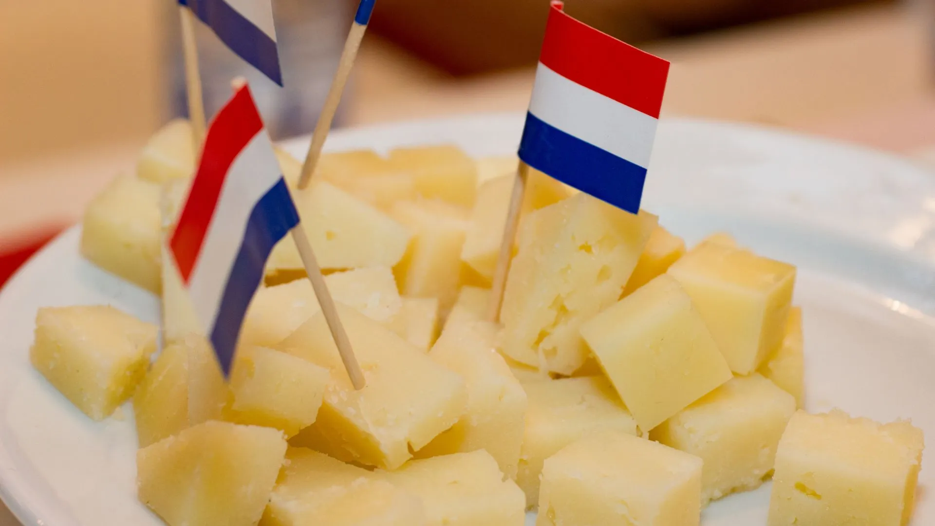 Plate piled with cubes of yellow Dutch cheese, several topped with small Dutch flags on toothpicks