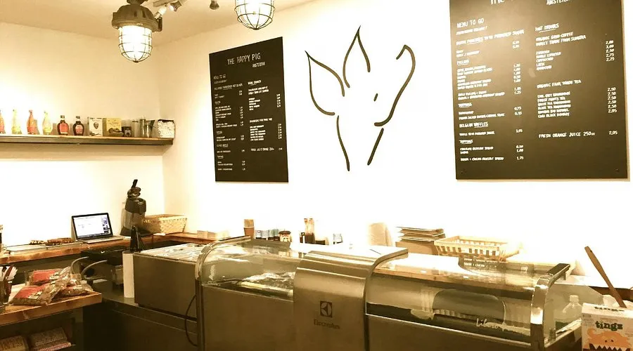 Small pancake shop interior with a pig logo on the wall, blackboard menus and a stainless steel counter