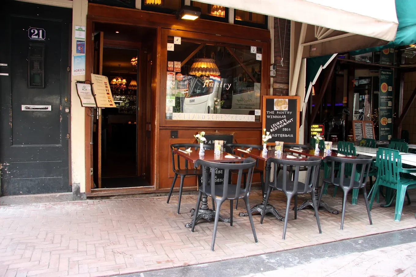 Dutch restaurant exterior with dark wood front, stained glass lamps inside and small terrace tables set with menus on the sidewalk